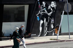People wearing masks walk past a mural depicting a coronavirus theme in Los Angeles, April 14, 2020.