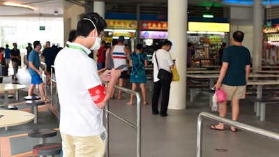 A safe-distancing enforcement officer wearing a red armband checks his phone at a food court in Singapore, April 18, 2020.