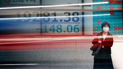 A woman wearing a mask stands near an electronic stock board showing Japan's Nikkei 225 index at a securities firm in Tokyo, April 24, 2020.
