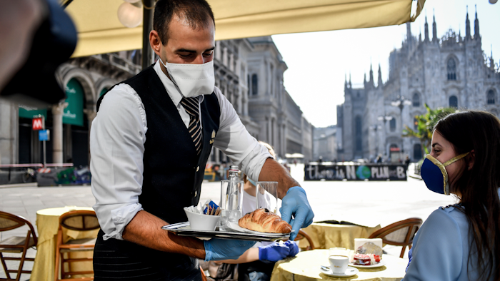 Two girls have breakfast served at a bar in front of the gothic Cathedral in Milan, May 18, 2020.