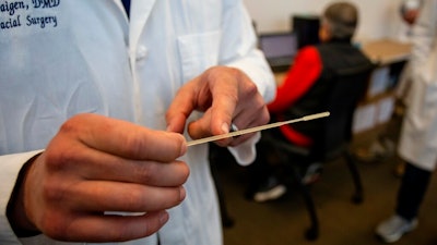 In this Tuesday, April 28, 2020, photo, Alexander Faigen, of Augusta University's Dental College of Georgia, shows how far a nasal swab must be inserted in Augusta, Ga. Volunteers at a Georgia dental college who started using a 3D printer to make nasal swabs used in test kits for the coronavirus are now a major part of the state's effort to expand testing.