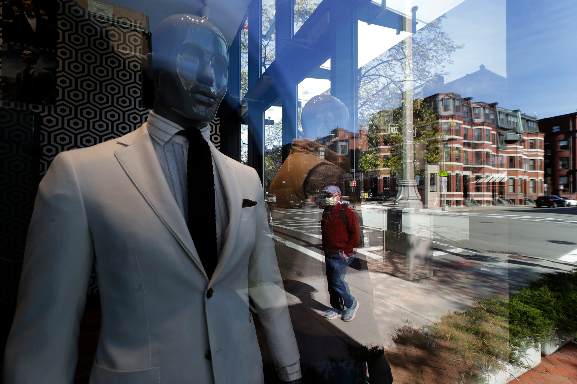 A passer-by wearing a mask out of concern for the COVID-19 coronavirus, background center, walks past mannequins in a clothing store in Boston.