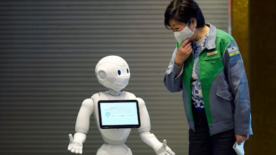 Humanoid robot Pepper, wearing a face mask, greets Tokyo Gov. Yuriko Koike in the lobby of a hotel for COVID-19 patients with mild symptoms, May 1, 2020, in Tokyo.