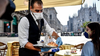 Two girls have breakfast served at a bar in front of the gothic Cathedral in Milan, May 18, 2020.