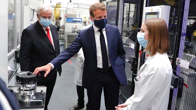 French President Emmanuel Macron, center, wearing a protective face mask, listens to explanations by an employee as CEO of France-based multinational automotive supplier Valeo Jacques Aschenbroicha looks on, in Etaples, , northern France, Tuesday May 26, 2020. Emmanuel Macron announced a 8 billion euro ($8.8 billion) plan to save the country's car industry from huge losses wrought by virus lockdowns, including a big boost for electric vehicles. The plan includes government subsidies for car buyers and longer-term investment in innovative technology, especially in battery-powered cars.