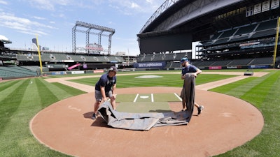 Grounds crew workers Jacob Weiderstrom, left, and Marcus Gignac pull a tarp off home plate at T-Mobile Park, Seattle, May 11, 2020.