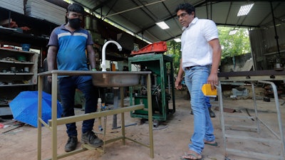 Nishantha Abeyrathne, right, checks a paddle sink at his workshop in Paththanduwana village, Sri Lanka, June 12, 2020.