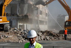 Greek Prime Minister Kyriakos Mitsotakis as bulldozers demolish an abandoned building behind him, Athens, July 3, 2020.