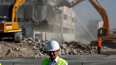 Greek Prime Minister Kyriakos Mitsotakis as bulldozers demolish an abandoned building behind him, Athens, July 3, 2020.