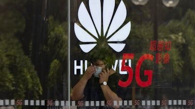 A worker wearing a mask speaks on the phone near the Huawei logo in a store in Beijing, July 15, 2020.