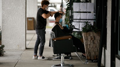 Hairstylist Travis Vu gives a haircut to Minh Dao at his outdoor hair salon in Fountain Valley, Calif., July 22, 2020.