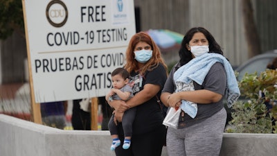 Two women and a child wait to take a coronavirus test at the Charles Drew University of Medicine and Science, July 22, 2020, in Los Angeles.