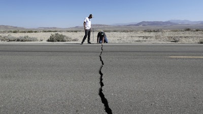 Ron Mikulaco, right, and Brad Fernandez examine a crack caused by an earthquake on Highway 178 outside Ridgecrest, Calif., July 6, 2019.