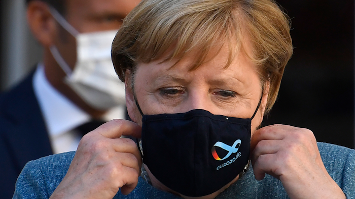 German Chancellor Angela Merkel takes her mask off as she arrives with French President Emmanuel Macron for a press conference at the Fort de Bregancon, France, Aug. 20, 2020.