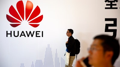 A man uses his smartphone as he stands near a billboard for Chinese technology firm Huawei at the PT Expo in Beijing, Oct. 31, 2019.
