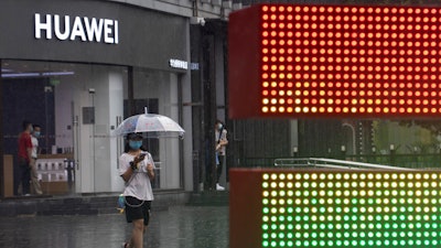 A woman wearing a mask to protect from the coronavirus walks with an umbrella as it rains outside a Huawei store.