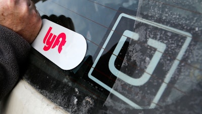 A Lyft logo is installed next to an Uber sticker in Pittsburgh, Jan. 31, 2018.