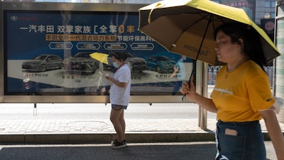 Residents pass an advertisement for Toyota hybrid cars, Beijing, Aug. 4, 2020.