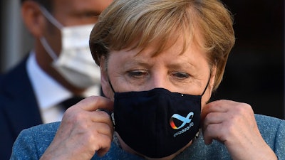 German Chancellor Angela Merkel takes her mask off as she arrives with French President Emmanuel Macron for a press conference at the Fort de Bregancon, France, Aug. 20, 2020.
