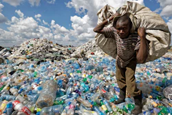 A man walks on a mountain of plastic bottles.