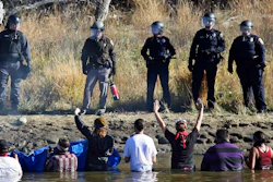 In this Nov. 2, 2016 file photo, dozens of protestors demonstrating against the expansion of the Dakota Access Pipeline wade in cold creek waters confronting local police, near Cannon Ball, N.D. The Army Corps of Engineers is recommending that the federal government negotiate a settlement with North Dakota for more than $38 million that the state spent policing the monthslong pipeline protests against the Dakota Access oil pipeline almost four years ago.
