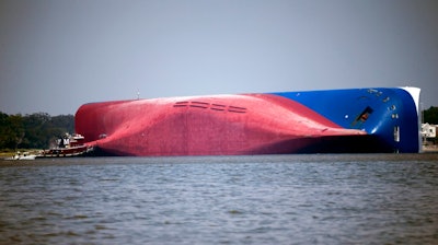 In this Sept. 9, 2019, file photo, a Moran tugboat nears the stern of the capsizing vessel Golden Ray near St. Simons Sound off the coast of Georgia. The salvage team is seeking a federal permit to surround the shipwreck with a giant mesh barrier to contain any debris when they cut the ship apart. Salvage workers coming to the Georgia coast to cut apart and remove the cargo ship that overturned will be isolated at a nearby resort to protect them from the coronavirus, officials said Tuesday, Sept. 8, 2020.