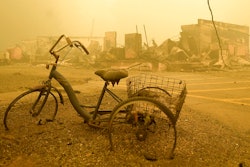 A trike stands near the burnt remains of a building destroyed by a wildfire.