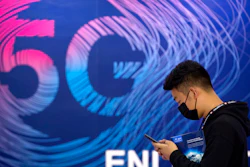 A man looks at his smartphone as he walks past a sign advertising 5G services at the PT Expo in Beijing.
