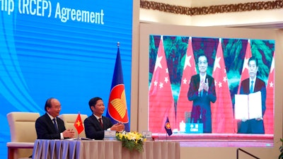 Vietnamese Prime Minister Nguyen Xuan Phuc, left, and Minister of Trade Tran Tuan Anh applaud next to a screen showing Chinese Premier Li Keqiang and Minister of Commerce Zhong Shan holding up the signed RCEP agreement, Hanoi, Nov. 15, 2020.