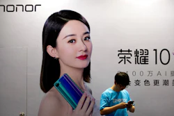 A staff member uses his smartphone in front of a billboard for Chinese smartphone brand Honor at the Global Mobile Internet Conference in Beijing, April 26, 2018.
