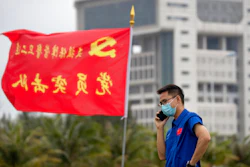 A worker talks on a cellphone near a flag with the logo of the Communist Party of China at the Wenchang Space Launch Site in Wenchang in southern China's Hainan province, Monday, Nov. 23, 2020. Chinese technicians were making final preparations Monday for a mission to bring back material from the moon's surface for the first time in nearly half a century — an undertaking that could boost human understanding of the moon and of the solar system more generally.