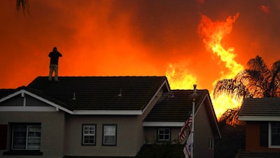 Herman Termeer, 54, stands on the roof of his home as the Blue Ridge Fire burns along the hillside in Chino Hills, Calif., Oct. 27, 2020.