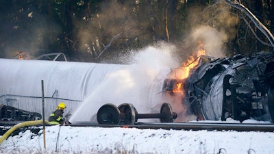 A firefighter sprays foam on a burning, derailed train car Tuesday, Dec. 22, 2020, in Custer, Wash. Officials say seven train cars carrying crude oil derailed and five caught fire north of Seattle and close to the Canadian border. Whatcom County officials said the derailment occurred in the downtown Custer area, where streets were closed and evacuations ordered during a large fire response.