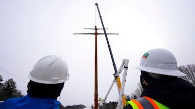 Workers watch the installation of the first pole of Central Maine Power's controversial hydropower transmission corridor near The Forks, Maine, Feb. 9, 2021.