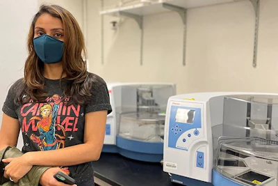 Smruthi Karthikeyan, PhD, stands next to the liquid-handling robotic platform that has made wastewater surveillance faster and cheaper.