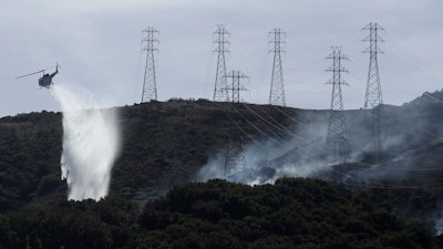 A helicopter drops water near power lines and electrical towers while working at a fire on San Bruno Mountain near Brisbane, Calif., Oct. 10, 2019.