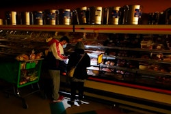 In this Tuesday, Feb. 16, 2021 file photo, customers use the light from a cell phone to look in the meat section of a grocery store that was without power, in Dallas. Brazos Electric Power Cooperative Inc., the oldest and biggest generation and transmission power cooperative in Texas has filed for Chapter 11 bankruptcy protection following last month’s winter storm that left millions without power.