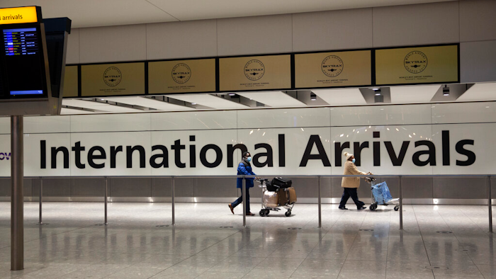 Passengers walk past a sign in the arrivals area at Heathrow Airport, London, Jan. 26, 2021.