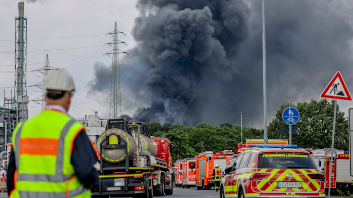 Emergency vehicles near an access road to the Chempark, over which a dark cloud of smoke is rising, Leverkusen, Germany, July 27, 2021.
