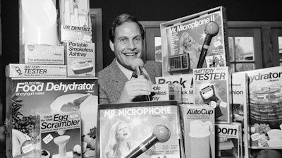 In this Wednesday, Dec. 8, 1982 file photo, Ron Popeil, the man behind those late-night, rapid-fire television commercials that sell everything from the Mr. Microphone to the Pocket Fisherman to the classic Veg-a-Matic, sits surrounded by his wares in his office in Beverly Hills, Calif. Ron Popeil, the quintessential TV pitchman and inventor known to generations of viewers for hawking products including the Veg-O-Matic, the Chop-O-Matic, Mr. Microphone and the Showtime Rotisserie and BBQ, died Wednesday, July 28, 2021 his family said.