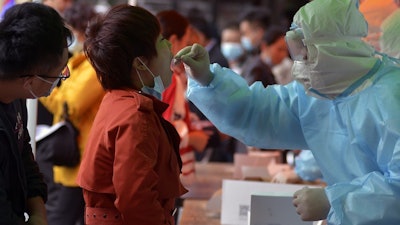 Medical staff takes a swab from a woman as residents line up for a COVID-19 test near a residential area in Qingdao, China, Oct. 12, 2020.
