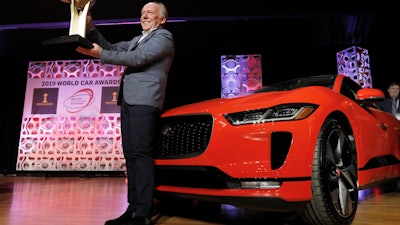 Jaguar Design Director Ian Callum raises the World Car of the Year trophy that was awarded to the Jaguar I-Pace, right, at the 2019 New York International Auto Show, April 17, 2019.