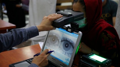 An employee scans the eyes of a woman for biometric data needed to apply for a passport, Kabul, Afghanistan, June 30, 2021.