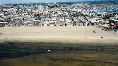 Workers in protective suits clean a contaminated beach in Newport Beach, Calif., Oct.6, 2021.