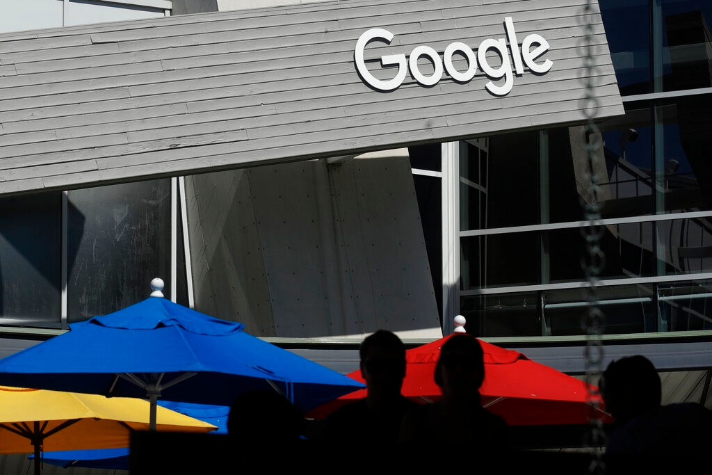 People walk by a Google sign on the company's campus in Mountain View, Calif., on Sept. 24, 2019. Google and Ford Co. are among those once again delaying their return-to-office plans, while other businesses whose workers are already back to the office are considering adding extra precautions like masks and doing COVID-19 testing.