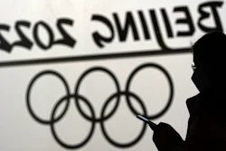 A woman looks at her phone as she passes an Olympic logo inside the main media center for the Beijing Winter Olympics, Jan. 18, 2022.