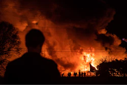 A bystander watches as Winston-Salem firefighters battle a structure fire at Weaver Fertilizer Co. on Monday, Jan. 31, 2022, in Winston-Salem, N.C.