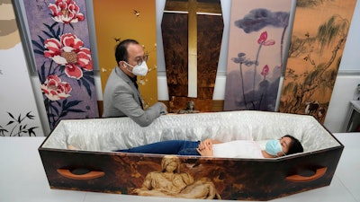 Wilson Tong, CEO of LifeArt Asia, left, talks to a reporter who tries out a catholic-designed paper coffin at Tong's factory in Hong Kong, March 18, 2022.