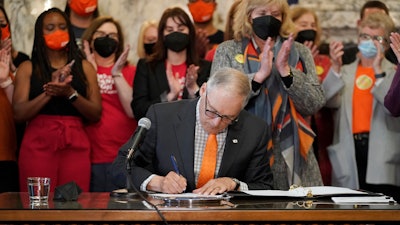 Washington Gov. Jay Inslee signs a bill that bans the manufacture, distribution and sale of firearm magazines that hold more than 10 rounds of ammunition at the Capitol in Olympia, March 23, 2022.