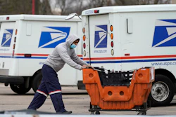 A United States Postal Service employee works outside a post office in Wheeling, Ill., Dec. 3, 2021. Four environmental groups that want the U.S. Postal Service to buy more electric delivery vehicles are suing to halt further purchases. The lawsuit, filed Thursday, April 28, 2022, in federal court in California, asks a judge to order the Postal Service to conduct a more thorough environmental review before moving forward with the next-generation vehicle program.